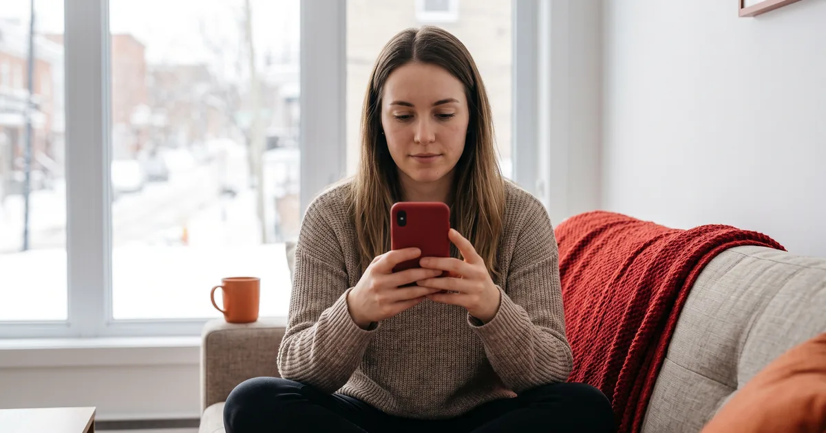 A young Canadian holding a phone and looking at an Instagram story in a bright Montréal apartment